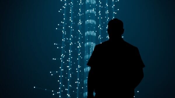 abstract silhouette of person from behind facing towering AI neural network structure, dramatic light contrast between human shadow and glowing technology, dark navy atmosphere, cinematic editorial photography, no text no letters no words no writing no signs no labels no watermarks no logos no typography no numbers on surfaces