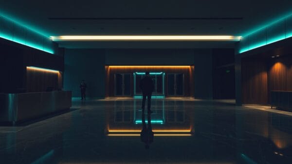 Hall d'entreprise vide au crépuscule, silhouette de dos au loin, sols en marbre et lumière verte.